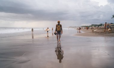 Yaz günü Bali 'de boş zamanlarını geçirirken kumlu sahilde bulutlu bir şekilde yürürken tanınmayan bir erkeğin arka plan görüntüsü.