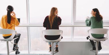 Gündelik kıyafetlerle birbirine bakıp gülen ve masada oturup sohbet eden genç kız arkadaşların arka plandaki görüntüsü.