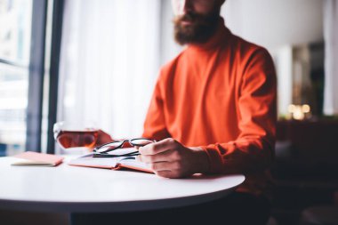 Düşük açılı günlük giysiler içinde bir bardak çay ve gözlüklü bir adam boş vakitlerinde masada oturuyor.