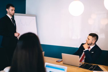 Yoğunlaşmış genç meslektaşlar dizüstü bilgisayarlara bakıyor ve modern konferans salonunda pazarlama stratejisini açıklayan erkek çalışanları dinliyor.