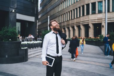 Tabletli mutlu bir adamın, modern binanın yanında dikilip omuzlarının üstünden sarkan cekete bakması.