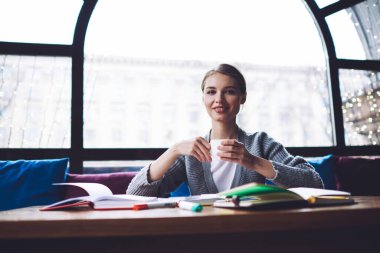 Saçlarını toplamış gülümseyen bayan öğrenci ara sırasında masada kahve içerken kameraya bakıyor.