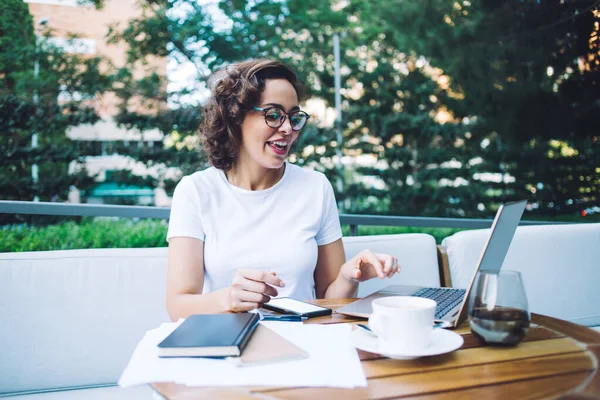 Beyaz gömlekli, gözlüklü, netbook ve akıllı telefon kullanarak gülümseyen genç bir kadın.