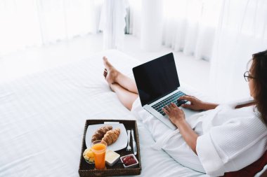 İnternette gezinirken ve Kuala Lumpur 'da yatakta uzanırken, dizüstü bilgisayarında daktilo kullanan, tanınmayan genç bir kadın.