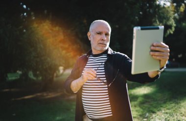  Gündelik giysiler içinde emekli bir adamın modern dokunmatik pedlere uygulama yüklerken kameraya bakması.