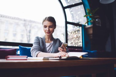 Gündüzleri rahat bir kafede çalışırken not defterlerinde kontrol notları ve akıllı telefonları karıştıran ciddi bir kadın.
