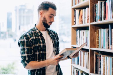 20 yaşındaki beyaz erkek öğrenci, kitapçıda bilgi kontrol edebilmek için edebiyat seçiyor.