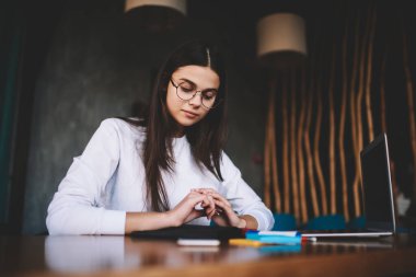 Tasarımın detaylarını düşünen düşünceli genç bir kız öğrenciden portatif bilgisayarlı rahat bir kafede otururken.