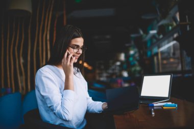 Beyaz günlük giysiler içinde gülümseyen serbest bir kadın. Gözleri açık bir şekilde masada otururken aşağıya bakıyor.
