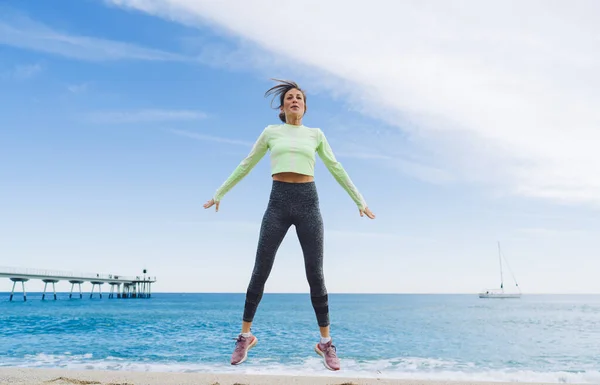 全身成熟した女性で活動中の女性とスニーカーは 青い空の背景にビーチでフィットネスワークアウト中に手を離れてジャンプします — ストック写真