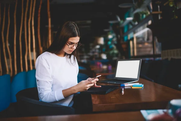 Pensive Female Freelancer Sitting Table Opened Laptop Using Smartphone While — Foto Stock