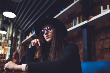 Kafeteryadaki masada oturup düşünürken şapkalı, sıradan siyah elbiseli ciddi bir kadının alçak açısı.