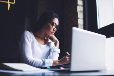 Modern çalışma ortamında netbook okuyup otururken ve ders çalışırken günlük giysiler içinde genç Afrikalı Amerikalı kız öğrenci notlar alıyor.