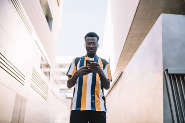 Sıradan giyinmiş, gözlüklü, akıllı telefondan arkadaşıyla sohbet eden Afro-Amerikan bir erkek. 