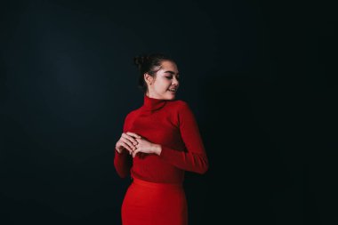 Parlak modaya uygun giyinmiş, gözleri kapalı ve elleri katlanmış, stüdyoda siyah arka planda dikilirken başını çeviren ürkek bir kadın model.