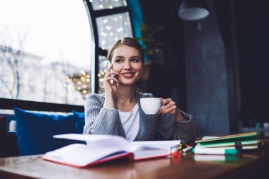 Gündelik kıyafetlerle gezen, gülümseyen ve gözlerini kaçıran, elinde not defterleriyle oturmuş akıllı telefonla konuşan ve kahve içen pozitif kadın bir serbest yazar.