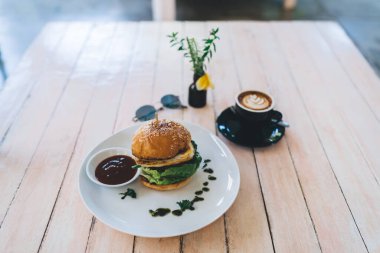 İştah açıcı taze burgerin, soslu aromatik kahvenin ve gün içinde kafedeki ahşap masanın üzerine koyulan latte sanatı.
