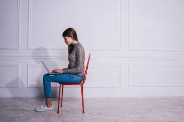 Modern çalışma ortamında dizüstü bilgisayar kullanırken gündelik kıyafetli, sandalyede oturan ve proje üzerinde çalışan genç kadın çalışanın yan görüntüsü