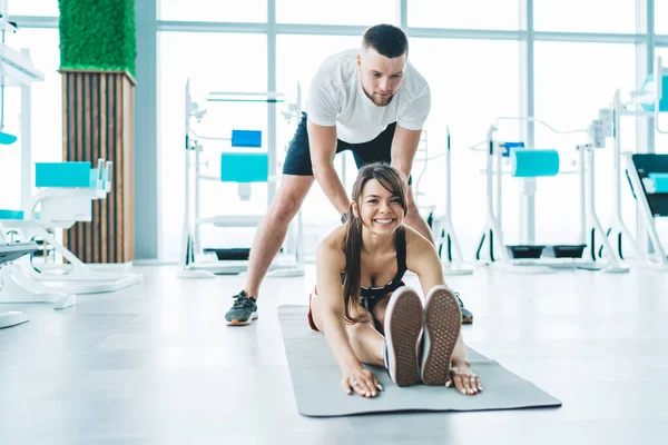 Serious Focused Trainer Helping Young Cheerful Smiling Sportswoman Stretching Mat — Stockfoto