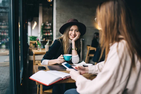 穿着时髦衣服的快乐的女性朋友们坐在木制桌旁 一边谈论着计划 一边一起享用热咖啡 — 图库照片