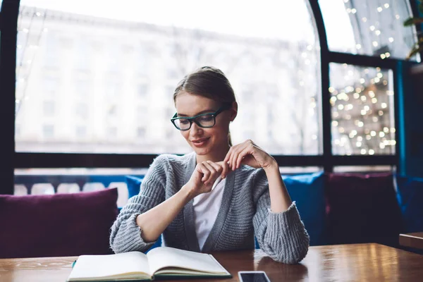 Mladá Pozitivní Žena Neformálním Oblečení Brýlemi Dívá Dolů Zatímco Sedí — Stock fotografie
