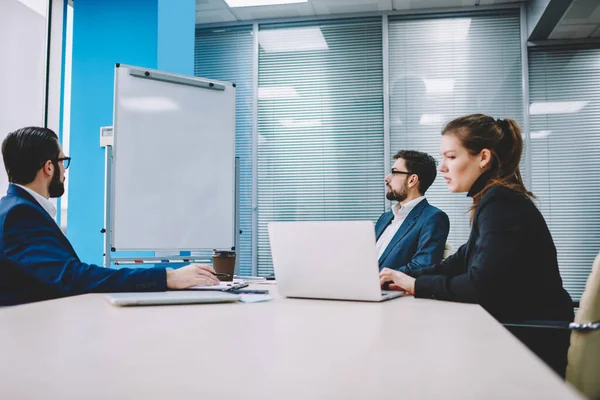 Resmi giysiler içinde bir grup düşünceli iş arkadaşı konferans masasında oturmuş modern ofiste projenin detaylarını tartışıyorlar.