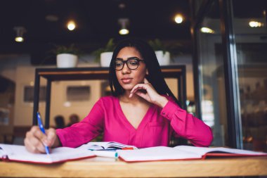 Uzun saçlı, gözlüklü, boynuna dokunan ve kafede sınava hazırlanan siyahi kız öğrencilerden.