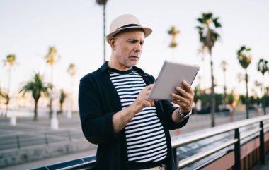  Yaşlı erkek turist emekliliğinde 4g kablosuz ağ kullanarak modern dokunmatik tabaka üzerinden sosyal medyada geziniyor