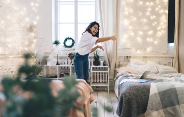 Neşeli kadın cep telefonuyla video görüşmesi yapıyor. Sıcak bir odada, duvarında parlak ışıklarla dikilirken.