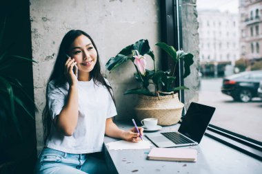 Telefonla konuşan, not alan, kafede ödevlerini yapan ve gözlerini kaçıran Asyalı genç kız öğrenci.