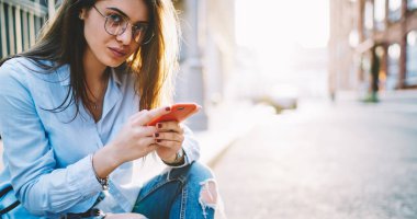 Görüntü koruması için şık gözlüklü genç bir kadının portresi elinde bloglar için akıllı telefonu tutan kameraya bakıyor.