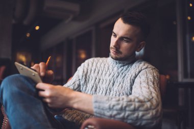 Düşünceli, sakallı, günlük giysiler içinde rahat koltukta oturan ve kafedeki not defterine not alan bir adamdan.