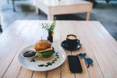 Yukardaki ahşap masadan lezzetli burger ve kahve fincanı ile latte sanatının yanında gündüz kafede siyah ekran ile birlikte.