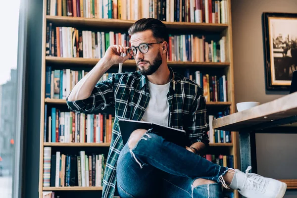 光学アイウェアの普及した男性ジャーナリストは 書店で勉強する組織計画を考慮して目の補正を提供します — ストック写真