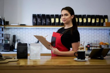 Kafeteryadaki barda ticari perakende hesaplarını denetleyen planlayıcısı olan kendine güvenen beyaz kadın barmen.