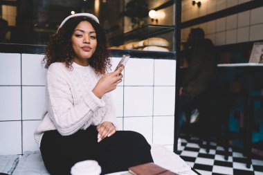 Modayı takip eden esmer tenli kadın portresi, elinde cep telefonuyla kafenin içinde blog yazarken istifa ediyor.