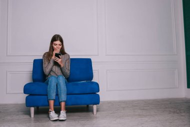 Gündelik kıyafetlerle gezen, iyi haberlerin tadını çıkaran ve kanepede otururken cep telefonunun ekranına bakan sürpriz kadın.
