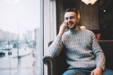 Rahat koltukta oturan, rahat bir kafede rahat bir şekilde konuşan, günlük kıyafetleri ve gözlükleriyle pozitif sakallı bir adam.