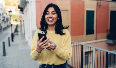 Kulaklıklarda mutlu Asyalılar. Müzik dinliyorlar ve internet sohbeti için akıllı telefonları kullanıyorlar.