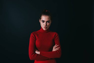 Karanlık arka plan ve katlanan eller üzerinde stüdyoda dururken kameraya bakıp surat asan ve dudak büken genç.