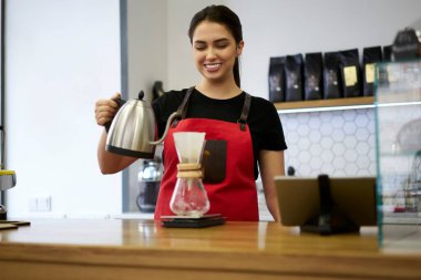 Kafeteryada filtre ve çaydanlık kullanarak kahve demlemekten hoşlanan önlüklü yetenekli kadın barista.