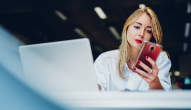 Düşük açılı, beyaz gömlek giyen, kırmızı rujlu, modern kafede oturan, uzaktan kumandalı, kırmızı tırnaklı bir kadın.