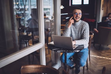 Neşeli, genç, serbest giyinen, gözlüklü, kameraya bakan ve akıllı telefondan konuşan bir adamdan.