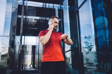 İş merkezinin girişinin yanında duran, akıllı telefondan sohbet eden ve akıllı saatlere bakan ciddi erkeklerin düşük açılı görüntüsü.