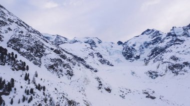 Soğuk kış gününde, doğada bulutlu gökyüzüne karşı karla kaplı kayalık sıradağlar.