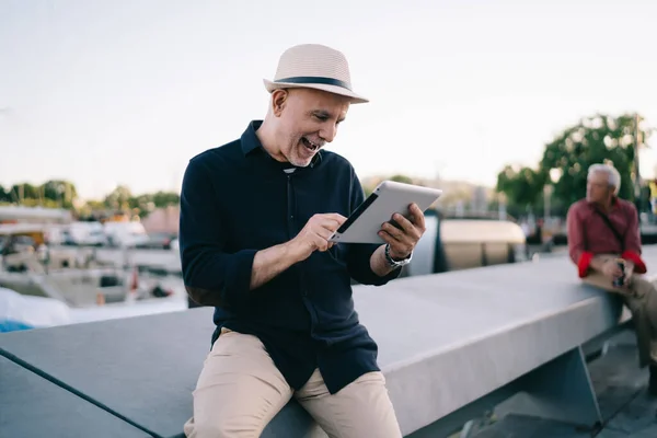 Happy male blogger 60 years old enjoying time for social networking during travel journey trip for recreating on retirement