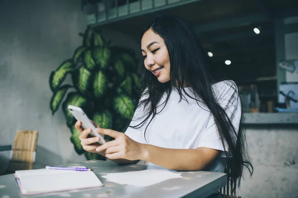 Gülümseyen Asyalı kız öğrencilerin akıllı telefondan mesaj atması ve kafede otururken not alması.