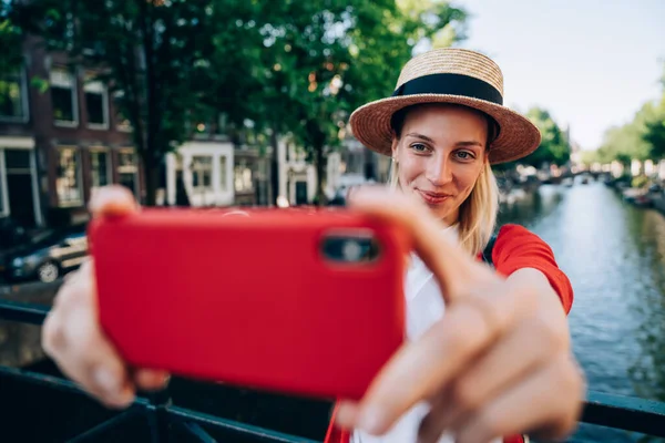 アムステルダムの緑の木々や運河で休暇中に橋の上に立っている間 携帯電話を使用して陽気な女性旅行者 — ストック写真