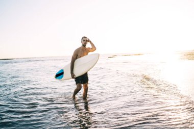 Okyanustaki spor antrenmanından sonra sahilde sörf yapan beyaz profesyonel sörfçü. Algarve 'de yaz tatilinin tadını çıkaran seksi genç adam.