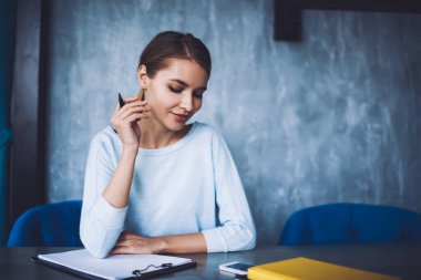 Genç serbest çalışan at kuyruklu, pano ile masada oturan ve çalışırken cep telefonunun ekranına bakan.